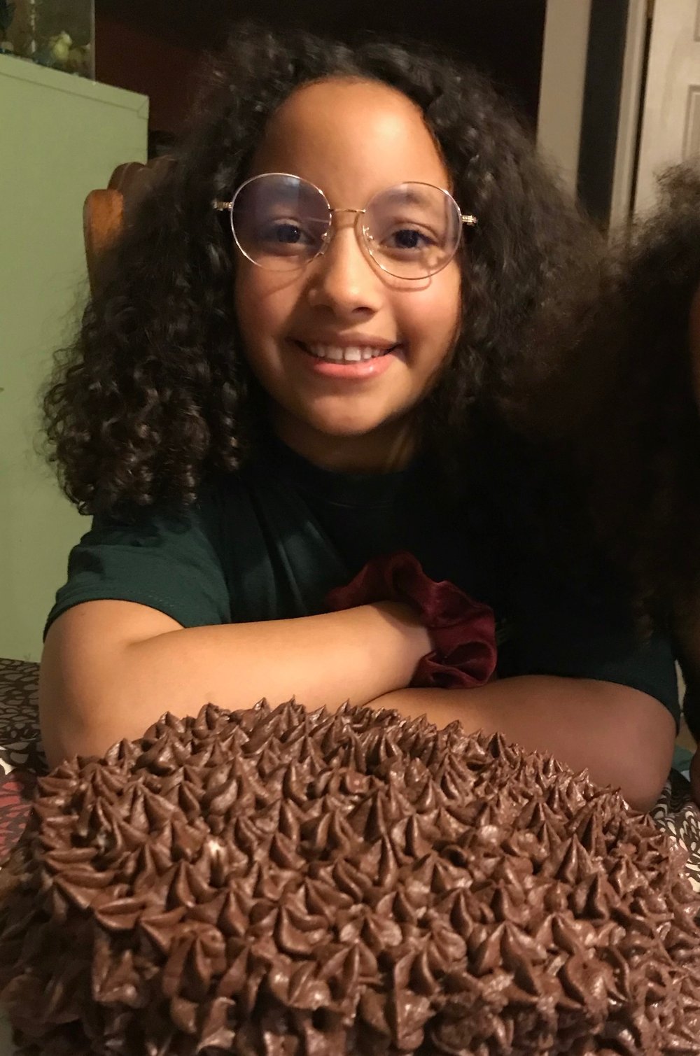 Evangeline smiling next to a chocolate-frosted cake she baked