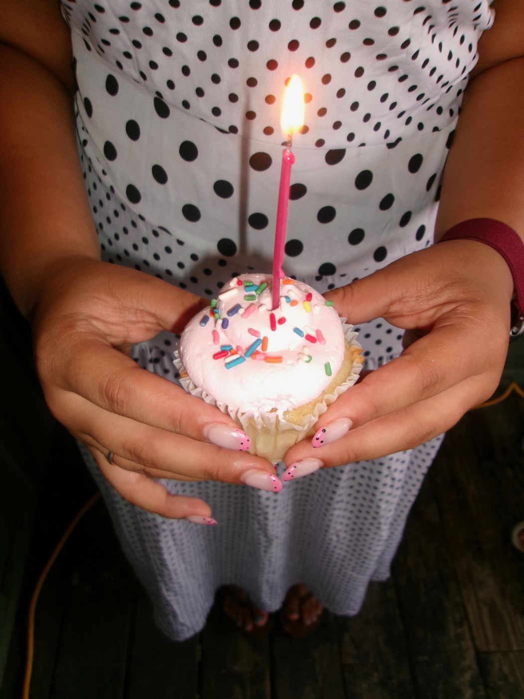 Hands holding a sprinkle cupcake with a lit candle