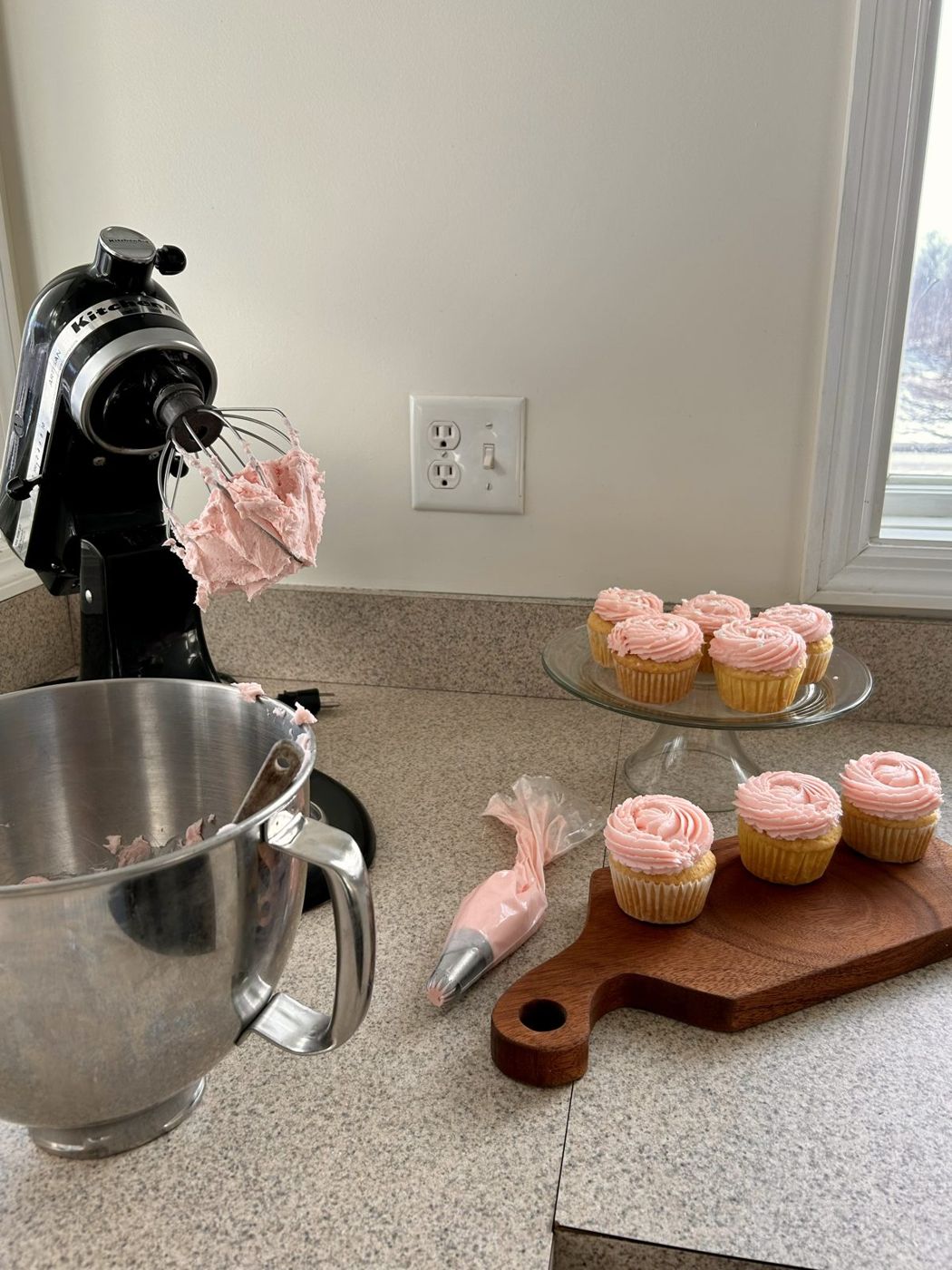 Pink frosted cupcakes next to a stand mixer in the kitchen