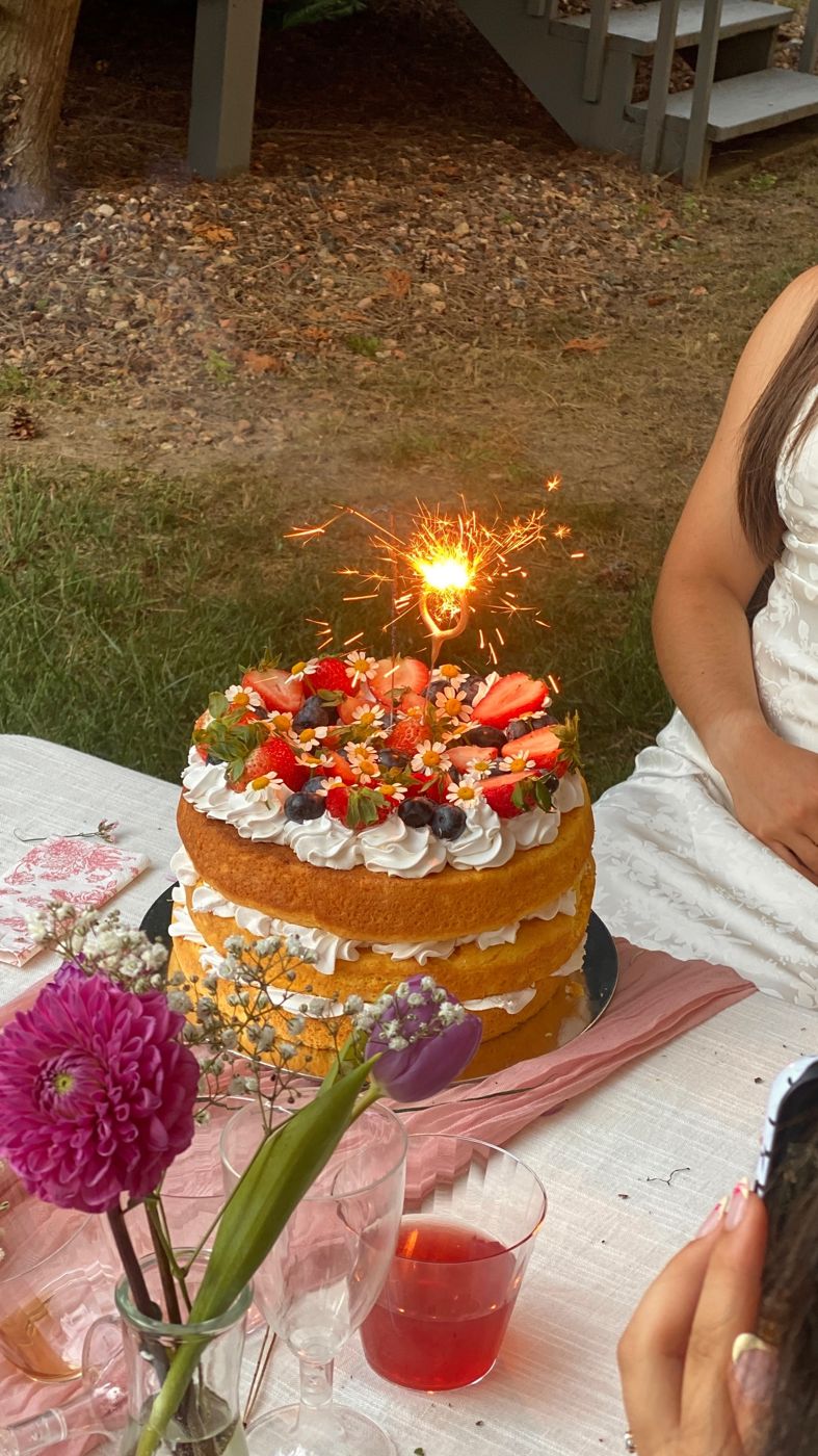Berry and daisy topped cake with a sparkler at an outdoor party
