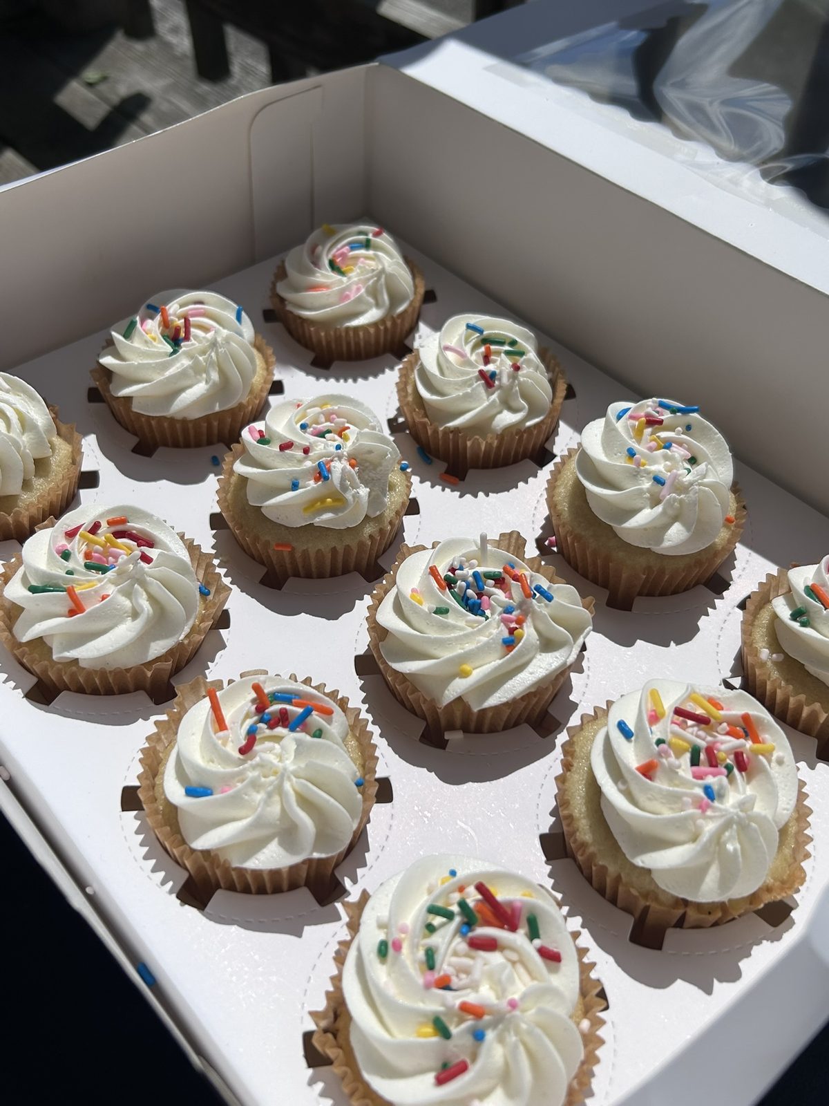 A box of vanilla cupcakes with buttercream swirls and sprinkles